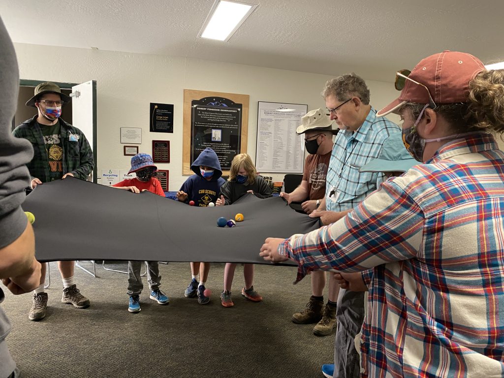 Demonstrating to kids how gravity in a black hole works by holding a blanket with some balls at the center